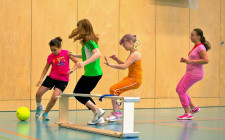 Vier junge Mädchen spielen Fussball, ein Schwedenkasten-Element ist das Tor. 