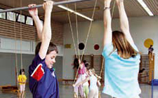 Deux enfants s'accrochent à une barre avec les mains, tandis que d'autres essaient différentes positions aux anneaux balançants.