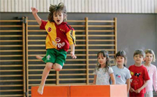 Un enfant saute par-dessus un obstacle sous les yeux de ses camarades.