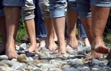 Delle persone a piedi nudi camminano su delle pietre in un piccolo torrente.