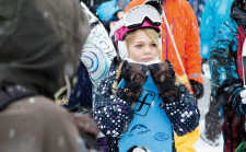 Une jeune fille tient sa planche dans ses mains et porte casque et lunettes de ski.