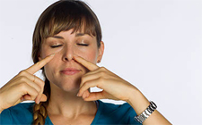 Junge Frau mit geschlossenen Augen, die durch ein Nasenloch atmet, während sie das andere mit dem Zeigfinger zuhält. 