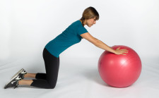 Une femme est à genoux, appuyée sur un ballon de gymnastique.