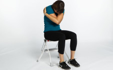 Une femme est assise sur une chaise et serre les bras devant soi.