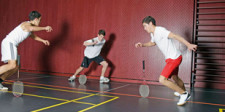 Tre giovani sono in cerchio, ognuno tiene una racchetta di badminton appoggiata verticalmente a terra.  