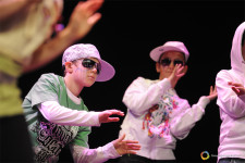 Dei bambini con un cappellino sulla testa e degli occhiali da sole battono il ritmo con le mani su un palcoscenico
