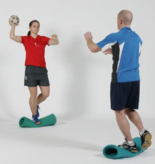 Deux athlètes sont en appui sur une une jambe sur une surface instable et se font des passes.