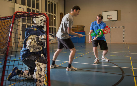 Aufnahme hinter dem Tor: ein Angreifer will schiessen, der Verteidiger will hindern, der Torhüter geht in die Knie.