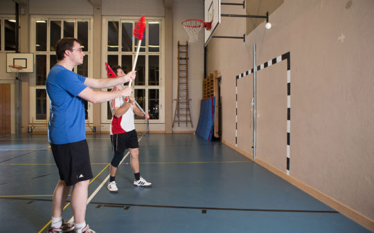 Zwei Spieler passen sich den Ball über eine Mauer zu.