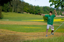 Un jeune homme est en position transversale sur une slackline tendue dans un champ.