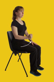 Una donna è seduta su una sedia e apre e chiude un pugno.