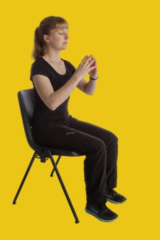 Una donna è seduta su una sedia con le punte delle dita unite e gli occhi chiusi.