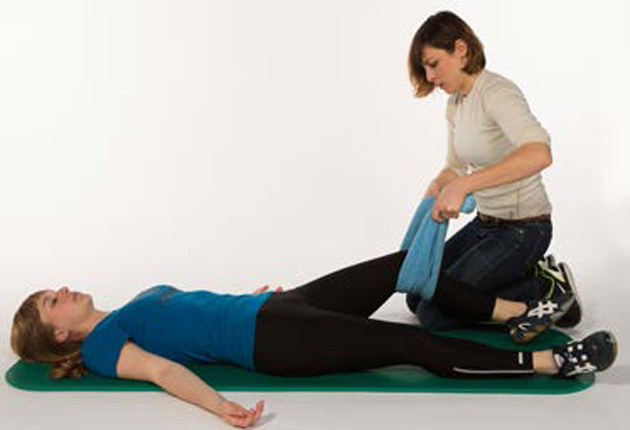 Una donna è sdraiata sulla schiena e un'altra le massaggia una gamba con l'ausilio di un asciugamano