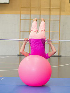Assise sur un swissball, une jeune fille effectue une montée au ventre à la barre.