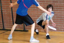 Un ragazzo lancia un frisbee cercando di farlo passare sotto il braccio di un avversario che lo sta marcando
