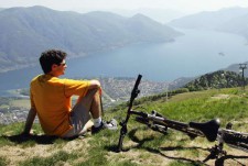 Un ragazzo è seduto su una montagna con accanto la mountainbike