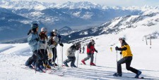 Schüler stehen auf einer Linie vis-à-vis von Skilehrer am Pistenrand und machen Aufwärmübungen.