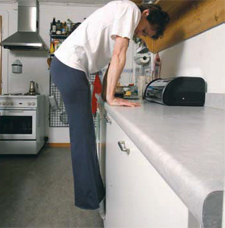 Una donna si solleva con le braccia appoggiate ad un piano di lavoro della cucina