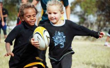 Un bambino e una bambina corrono con un pallone da rugby in mano.