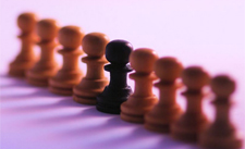 Symbolbild: Mehrere Schachfiguren in weiss, eine in schwarz.