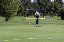Un giocatore di golf cerca di far volare una pallina fra due aste poste una sopra l'altra.
