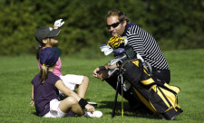 Ein Golftrainer erklärt sitzenden Kindern etwas über den Parcours.