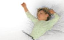 Un enfant est couché dans son lit, les bras tendus vers le haut.