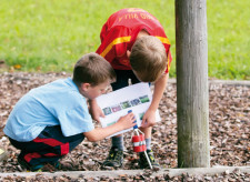 Due bambini a una postazione di corsa d'orientamento trascrivono delle lettere