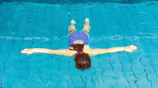 Kind schwebt mit Gesicht im Wasser bäuchlings auf Wasseroberfläche.