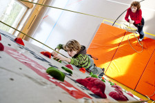 Un bambino si arrampica su una parete d'arrampicata mentre un adulto ai suoi piedi lo assicura con delle corde