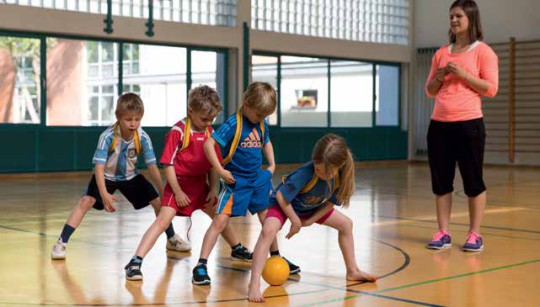 Kinder in einer Reihe und versuchen, einen Ball zwischen gegrätschten Beinen hindurch zu spielen.