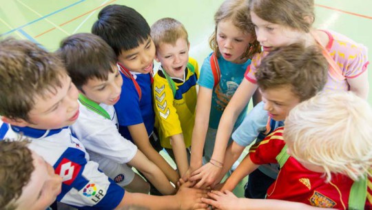 Foto: dei bambini sono in cerchio e ognuno allunga un braccio in mezzo al cerchio.