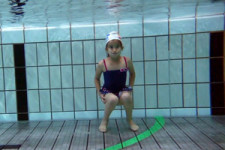 Une fille s'accroupit au fond de la piscine.