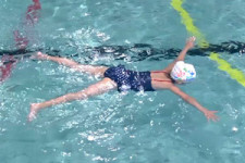 Una bambina galleggia nell'acqua sulla pancia con braccia e gambe divaricate