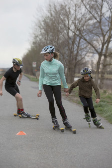 Trois enfants se déplacent avec des rollers ou des skis à roulettes.