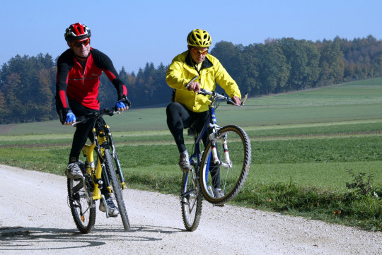 Zwei erwachsene Männer beim Mountainbike-Fahren auf einem Feldweg.