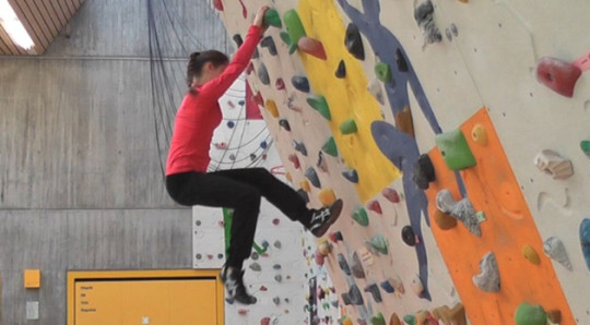 Une jeune fille grimpe à un mur sans corde.