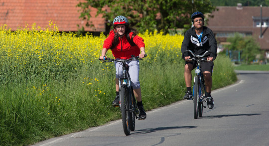 Zwei Jugendliche auf dem Fahrrad auf wenig befahrener Strasse.