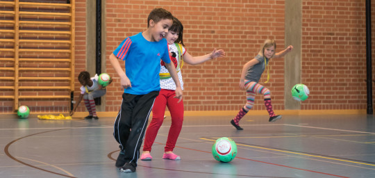 Dei bambini giocano con diversi palloni da calcio in una palestra.