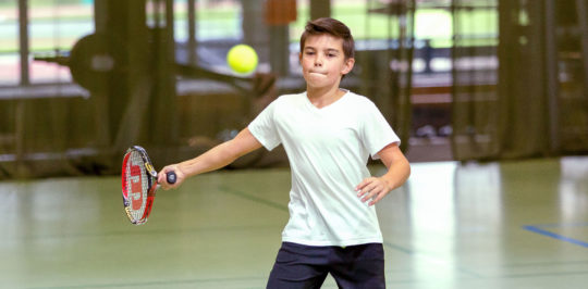 Un garçon frappe une balle de tennis en coup droit.