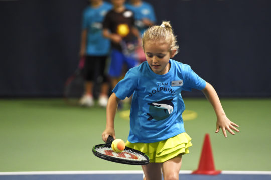 Mädchen balanciert einen Tennisball auf einem Tennisschläger.