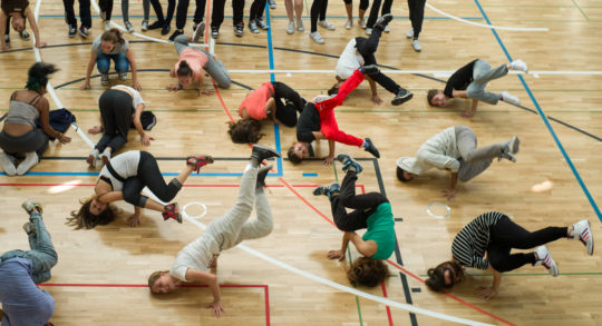 Schülerinnen und Schüler machen einen Breakdance-Move in der Sporthalle.