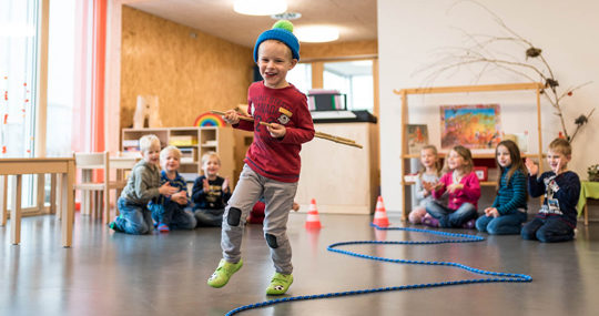 Foto: un bambino corre lungo una corda indossando un berretto invernale in un'aula di una scuola dell'infanzia