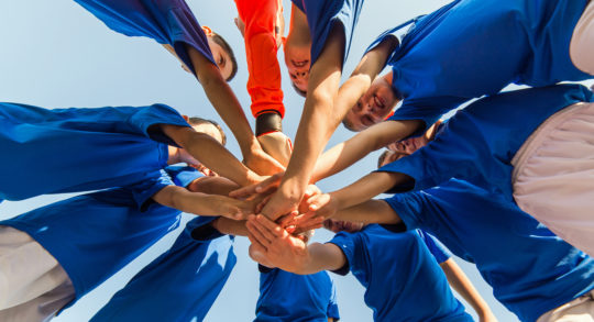 Foto: un gruppo di bambini in cerchio con un braccio teso verso il centro per eseguire un rituale prima o dopo una partita