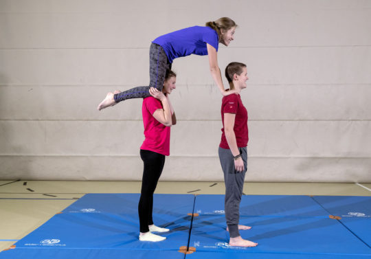 Une élève se tient en appui à quatre pattes sur les épaules de deux camarades.