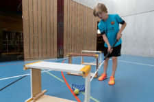 Foto: Schüler spielt durch Schwedenkastenelemente einen Tennisball mit Unihockeyschläger.