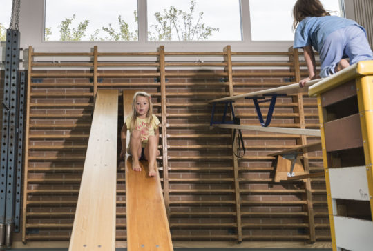 Foto: una bambina scivola su una panchina appesa alle spalliere, mentre un'altra si arrampica su una panchina inclinata