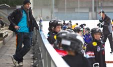 Photo: un parent suit un entraînement de manière passive à la bande d'une patinoire.