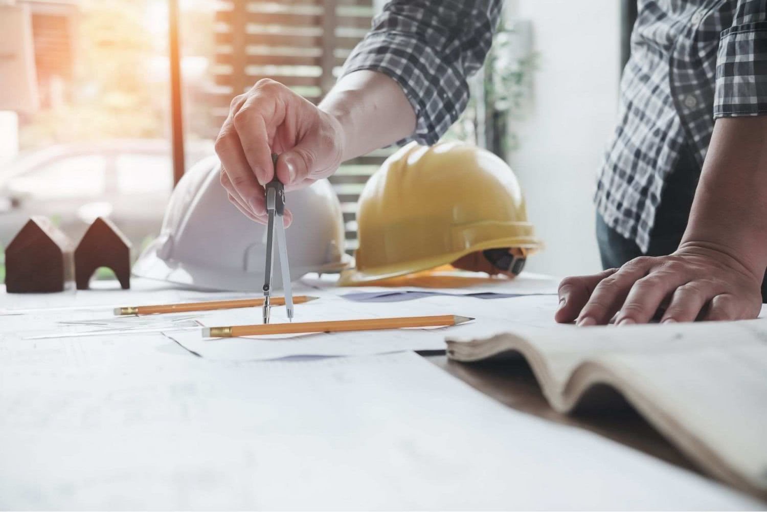 Architect with compass, construction plans, construction site helmet on table