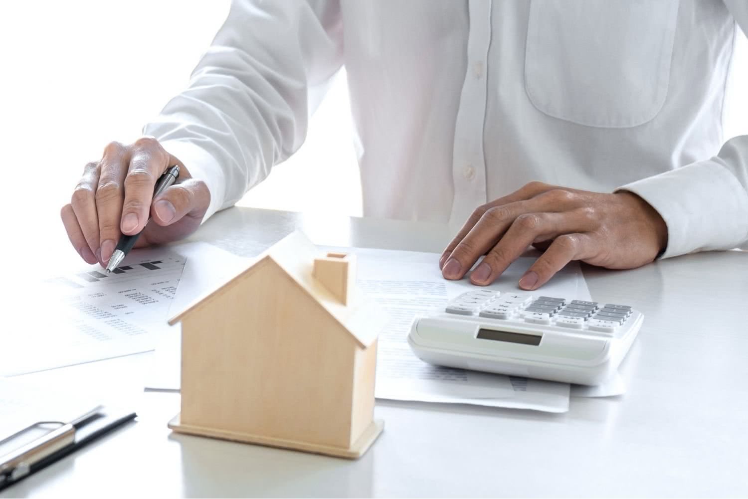 Man with calculator and wooden house on the table
